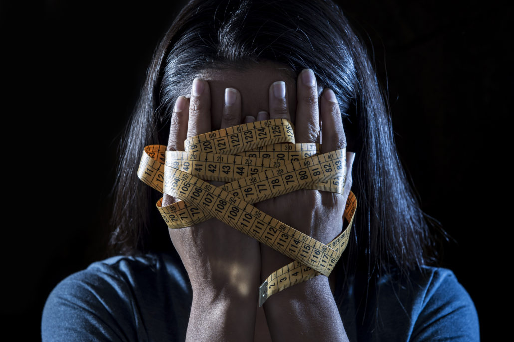 hands wrapped in tailor measure tape covering face of young depressed and worried girl suffering anorexia or bulimia nutrition disorder